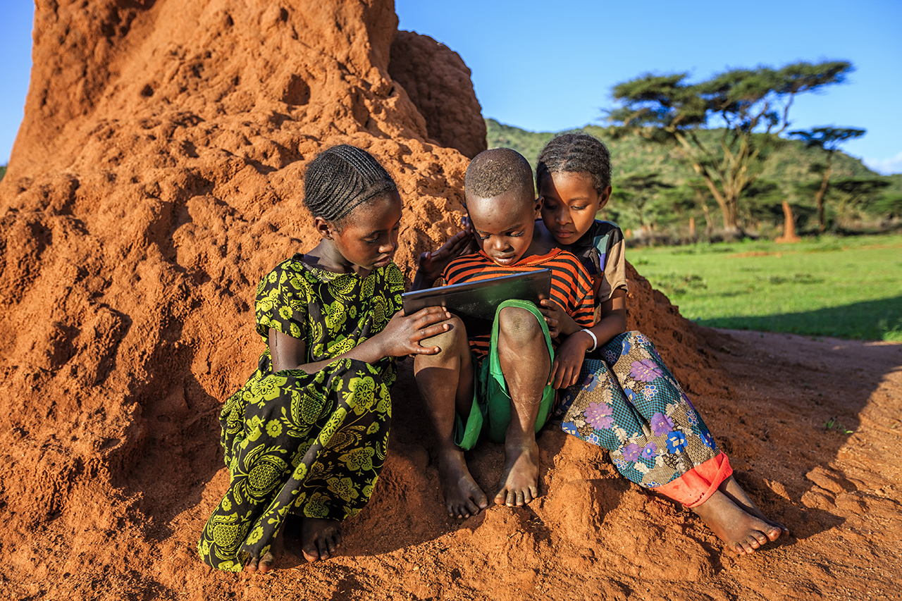 Three Ethiopian children using tablet outdoors.