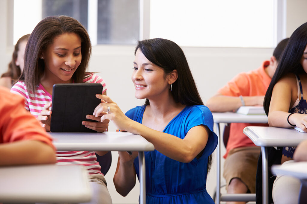 Teacher Helping Female High School Student In Classroom Using Tablet