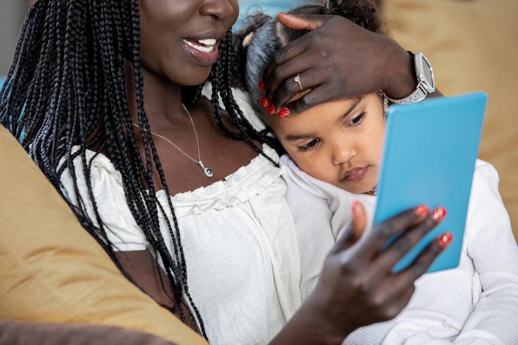 Mother and toddler sitting together looking at a tablet. 